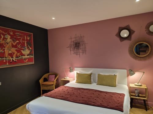 Chambre de luxe à l'Hôtel Du Cygne, Tours avec murs roses, lit double aux oreillers olive, fauteuil en rotin et éléments décoratifs