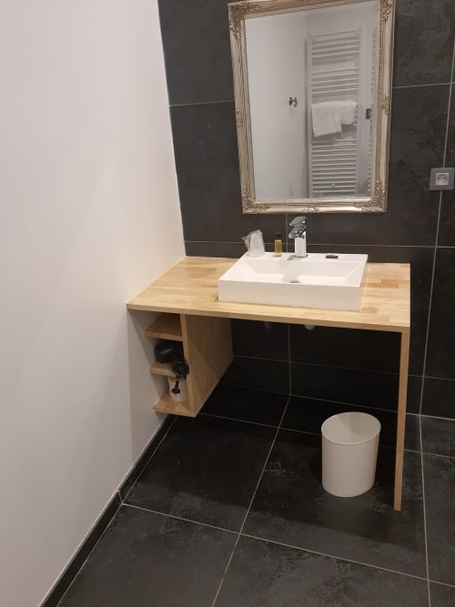 Salle de bains accessible avec vasque blanche, meuble en bois, miroir orné et carrelage noir à l'Hôtel Du Cygne à Tours