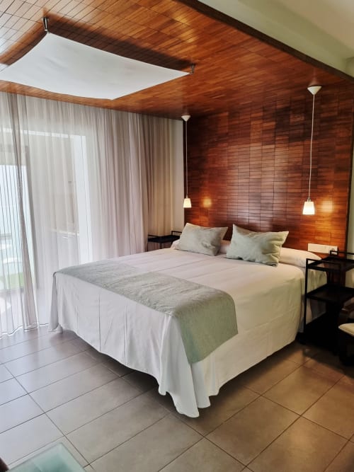 Modern bedroom at El Arrecife de Conil, Conil de la Frontera. Wooden accent wall, queen bed, pendant lighting, and glass