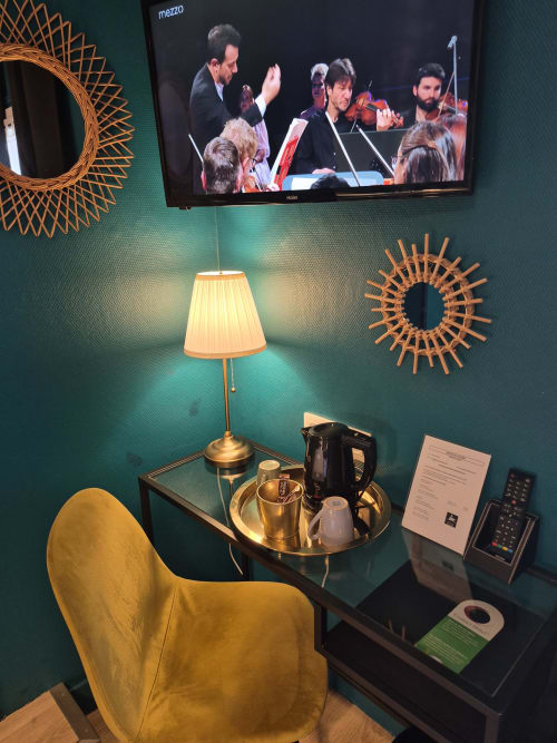 Chambre d'hôtel moderne à l'Hôtel Du Cygne Tours avec murs bleu-vert, fauteuil doré, lampe, miroirs décoratifs, TV diffusant un orchestre