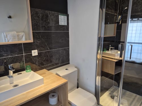 Salle de bain moderne de l'Hôtel Du Cygne à Tours avec carrelage en marbre noir, double vasque, toilettes et douche vitrée