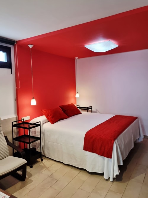Modern red accent wall bedroom at El Arrecife de Conil with double bed, pendant lights, and city view in Conil de la Frontera