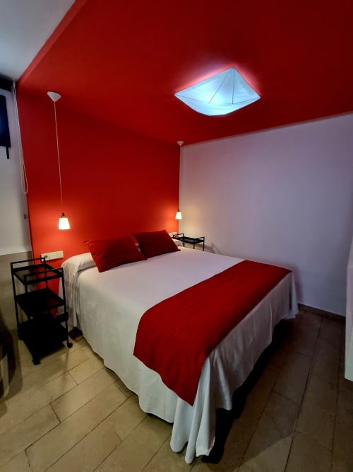 Modern bedroom at El Arrecife de Conil with red accent ceiling, double bed, pendant lighting, and contemporary design in