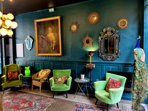 Le hall du Hôtel Du Cygne à Tours arbore des murs bleu-vert, du mobilier vintage, des miroirs soleil et une statue de paon décorative.