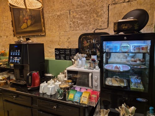 Station café de l'Hôtel Du Cygne Tours avec machine à espresso, présentoir de pâtisseries et sélection de thés sur le comptoir