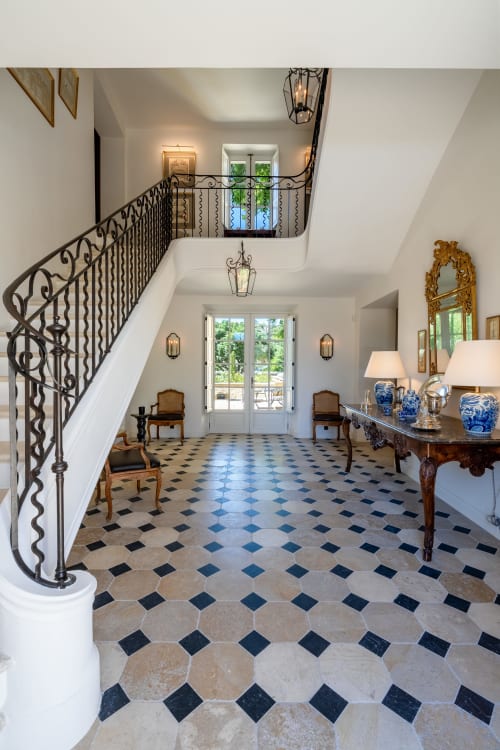 Elegante vestíbulo de dos plantas en Le Domaine du Fortin con escalera de hierro forjado, piso de azulejos de diamante y puertas francesas