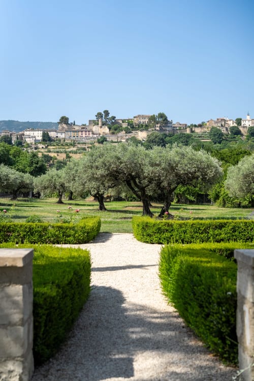 Sendero formal con setos y vista al pueblo de Ménerbes y olivares de Le Domaine du Fortin, Provenza