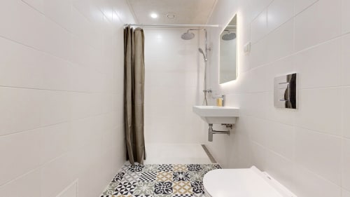 Modern white bathroom with geometric floor tiles, rainfall shower, sink with mirror, and brown shower curtain at tARTu Stays