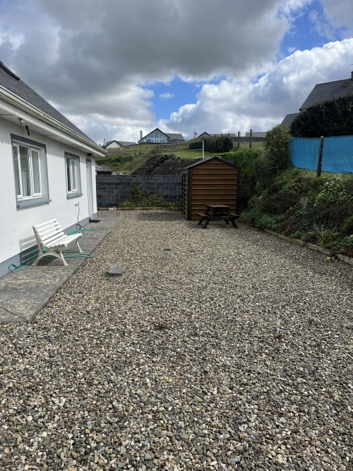 Gravel patio with white cottage, wooden shed, seating, and fenced garden at Bucket & Spade, Co. Clare