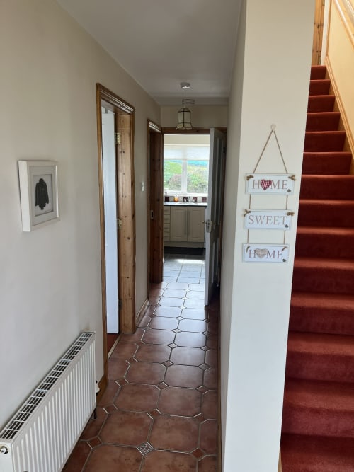 Hallway at Ard Na Mara apartment in Co. Clare with terracotta tiles, staircase, and Home Sweet Home sign