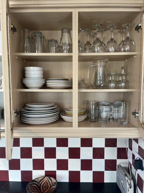 Open kitchen cabinet in Ard Na Mara apartment at Bucket & Spade, Co. Clare, displaying stacked plates, glassware, and dining