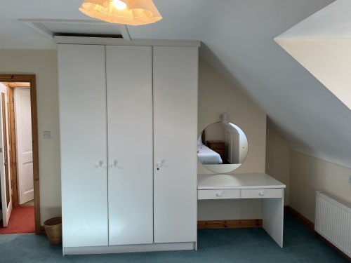Attic bedroom at Bucket & Spade, Co. Clare with white wardrobes, vanity mirror, and desk in Ard Na Mara apartment