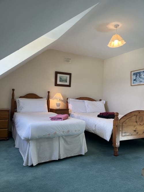 Cozy attic bedroom at Bucket & Spade, Co. Clare with two wooden beds, white linens, and warm pendant lighting.