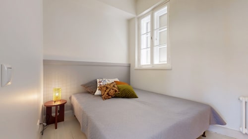 Bright, minimalist bedroom at tARTu Stays in Tartu with queen bed, colorful pillows, bedside lamp, window with city view, and
