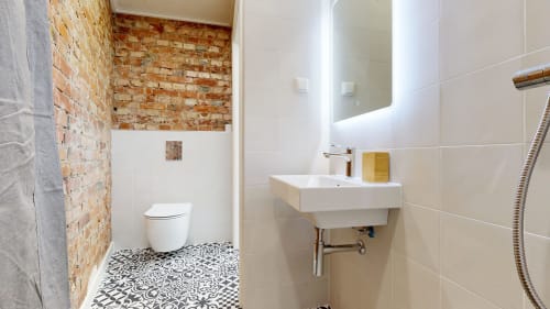 Modern bathroom in tARTu Stays apartment with white sink, toilet, exposed brick accent wall, and patterned floor tiles