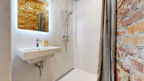 Modern bathroom at tARTu Stays with white tiles, illuminated mirror, wall-mounted sink, and exposed brick accent wall