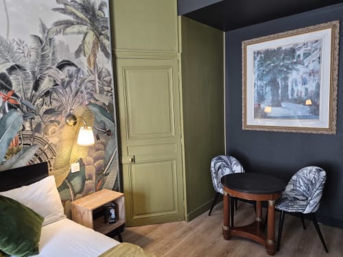 Chambre de l'Hôtel Du Cygne Tours avec papier peint tropical, porte verte panelée, table ronde, chaises à motifs et œuvres encadrées