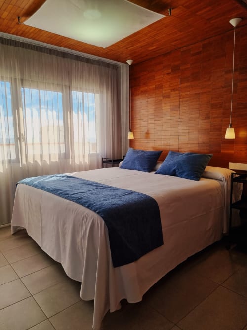 Modern bedroom with wooden walls, blue pillows, beige bedding, and sea view balcony at El Arrecife de Conil hotel in Cádiz