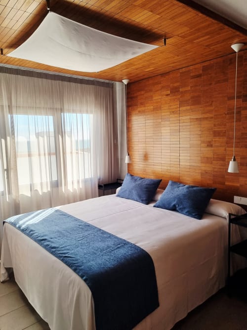 Modern bedroom at El Arrecife de Conil with wood-paneled walls, queen bed with blue accents, sea view balcony, and