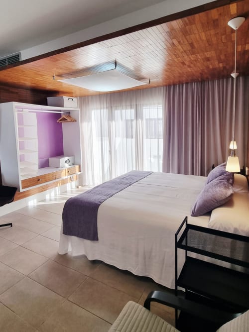 Modern bedroom at El Arrecife de Conil in Cádiz with purple accents, wooden ceiling, double bed, and city view