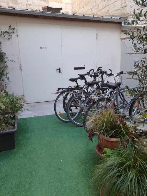 Vélos stationnés dans la cour de l'Hôtel Du Cygne à Tours, avec portes de garage blanches et plantes en pot