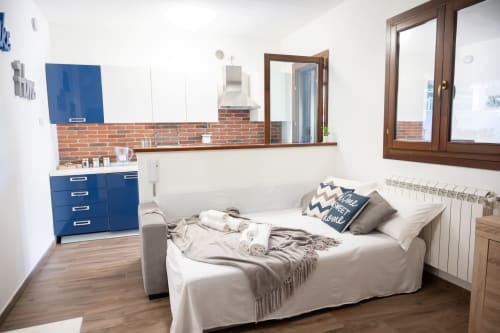Modern studio bedroom in Ferrara villa with blue kitchenette, white bed, brick backsplash, and sea view near beach