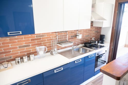 Modern blue kitchen with brick backsplash, stainless steel sink, gas cooktop, and white countertops in LikeHome Gelsomini