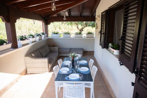 Shaded patio dining area with table set for six, wicker seating, and potted plants in villa near Ferrara, Italy