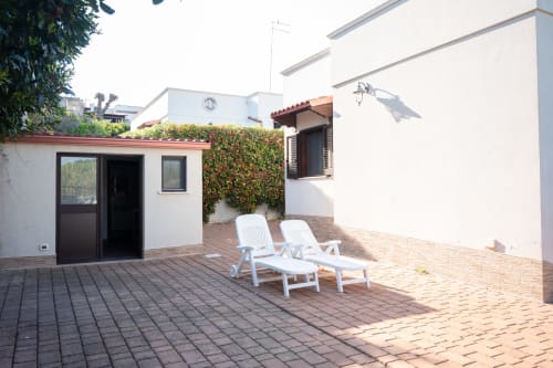 Sunny terrace of LikeHome Gelsomini villa near Ferrara with white loungers, brick patio, and white-walled accommodation