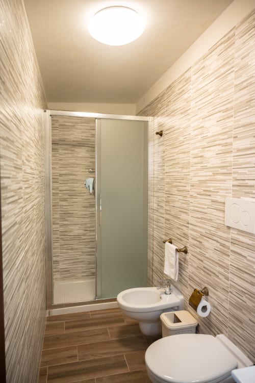 Modern bathroom with beige striped tile walls, walk-in shower, toilet, bidet, and sink in LikeHome Gelsomini villa near