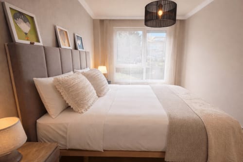 Dormitorio luminoso con cabecero acolchado gris, ropa de cama blanca y vistas al mar en la casa Holibai de Baiona