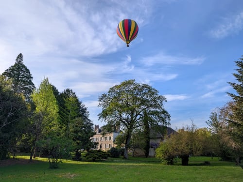Mongolfière colorée survolant le domaine du Clos Sainte-Marie à Mesland, France, avec ses espaces verts et architecture historique