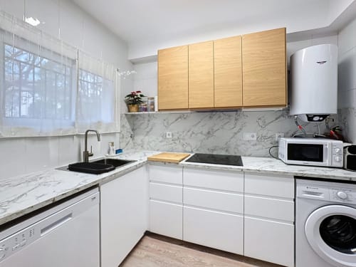 Cocina moderna de la casa Mar Blau en L'Estartit con gabinetes blancos, encimeras de mármol y armarios superiores de madera