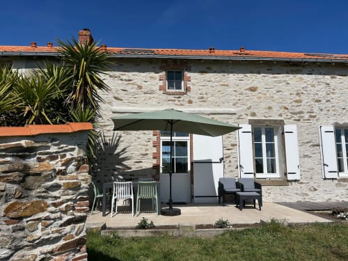 Tuinterras van Gîte Les Plages bij Le Pré d'Olonne, L'Île d'Olonne, met stenen cottage, groene parasol en zithoek