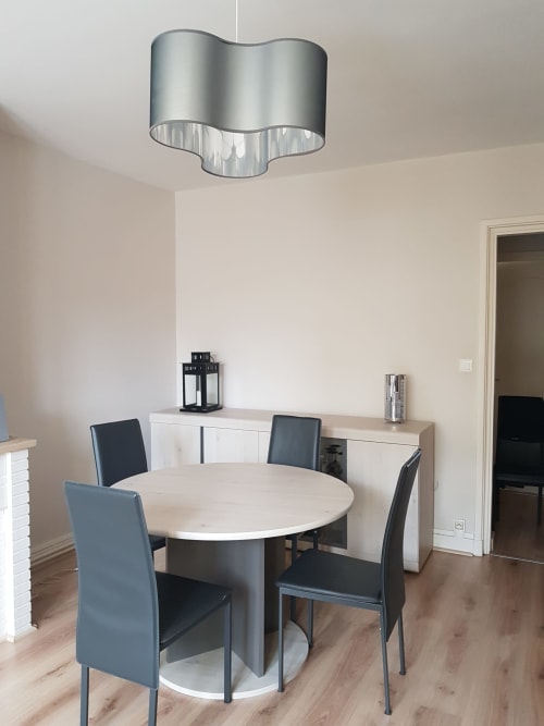 Salle à manger moderne dans un appartement à Dunkerque avec table ronde blanche, chaises noires et suspension argentée
