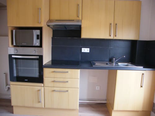 Cuisine moderne avec armoires en bois clair, plan de travail noir, évier inoxydable, micro-ondes et four dans un appartement à Dunkerque