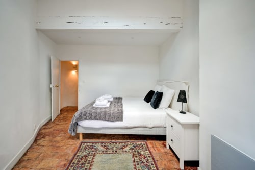 Suite Mirabeau bedroom at Les Suites de Montigny, Aix-en-Provence, with bed, nightstand lamp, and terracotta floor.