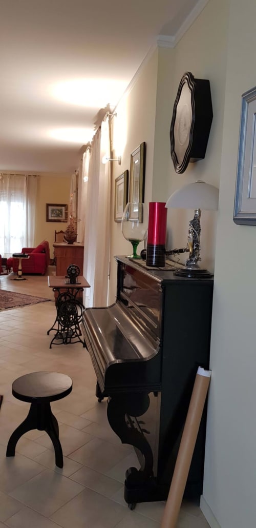 Elegante corridoio nell'appartamento Tales of Abruzzo con pianoforte nero, sgabello decorativo e zona living aperta con mobili rossi