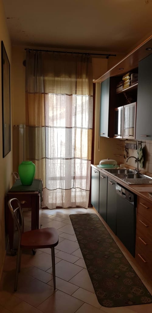Cucina luminosa dell'appartamento Tales of Abruzzo con lavello, fornello, tavolo da pranzo, vaso verde e tende a righe affacciate