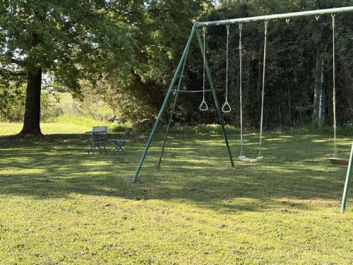Aire de jeux extérieure avec balançoires et barres de singe entourée d'arbres au gîte Le Jardin d'Elusa à Eauze, France