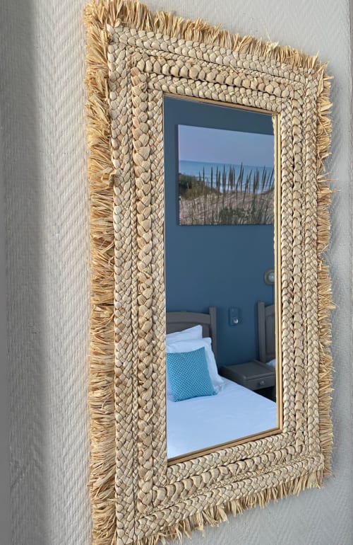 Woven straw-framed mirror reflecting bedroom with bed and landscape artwork at Hôtel Maison Richet, Les Sables-d'Olonne