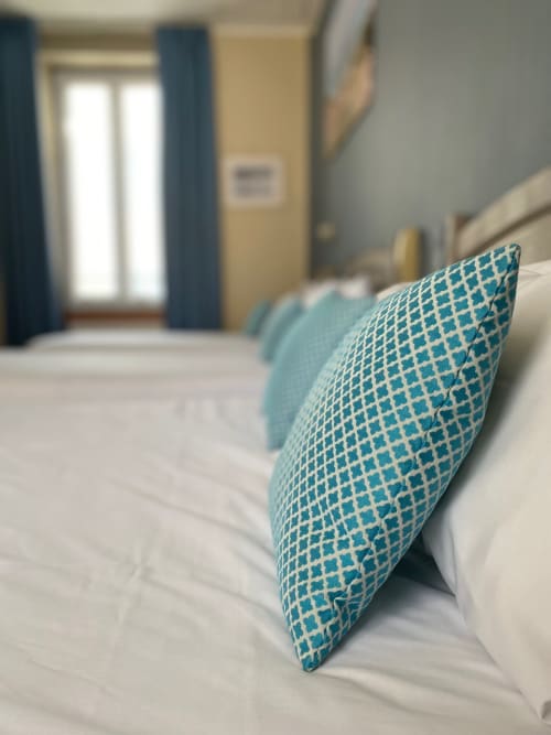 Turquoise patterned pillow on white bed in Hôtel Maison Richet room, Les Sables-d'Olonne