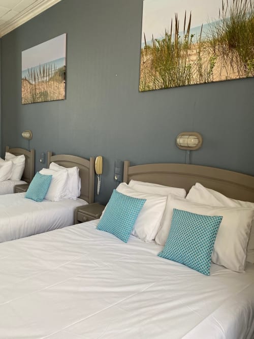 Coastal-themed hotel room with two queen beds, turquoise pillows, beach grass artwork, and gray walls at Hôtel Maison Richet