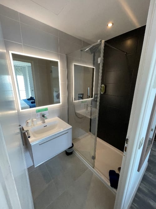 Salle de bain moderne avec miroir lumineux, lavabo blanc et douche à l'italienne à l'Hôtel Flots d'Azur à Nice
