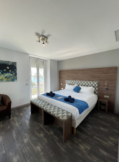 Chambre moderne de l'Hôtel Flots d'Azur à Nice avec balcon vue mer, tête de lit en bois et décor bleu