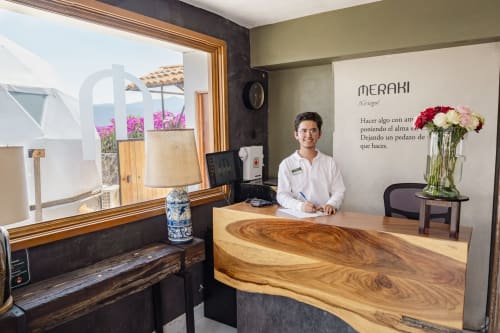 Recepcionista de hotel en la recepción de Meraki Glamping en Malinalco con mostrador de madera natural y vistas a las montañas