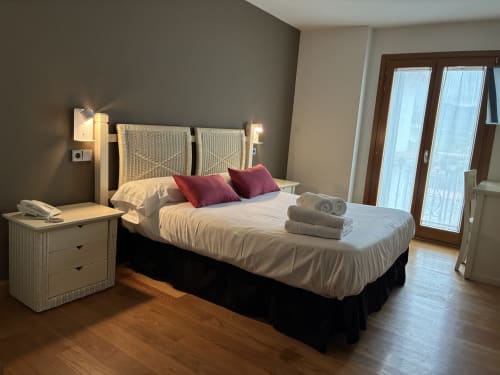 Moderno dormitorio doble en el hotel Casa Azcona con cabecero tejido, ropa de cama blanca impecable, almohadas burdeos y balcón acristalado
