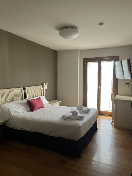 Modernes Doppelzimmer in Casa Azcona mit weißer Bettwäsche, Rattankopfteil, TV und Glastüren zur Balkonterrasse in Zizur