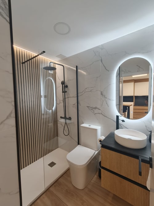 Baño moderno en Bahia Mar Canarias con paredes de mármol, ducha a ras de suelo, espejo iluminado y tocador de madera en Vista