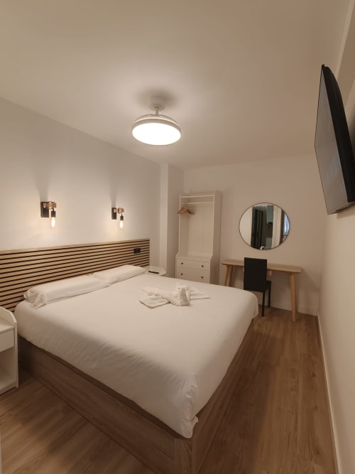 Habitación moderna del hotel Bahia Mar Canarias en Telde con cama matrimonial, espejo redondo, escritorio y lámpara de techo
